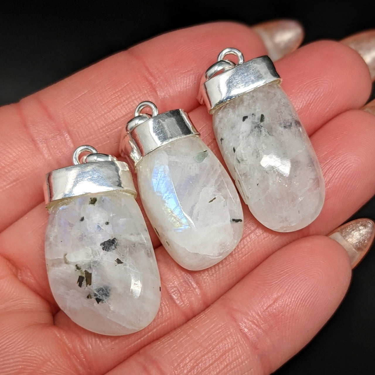 Close-up of a person holding crystal pendants, featuring Rainbow Moonstone AAA Tumbled Pendant