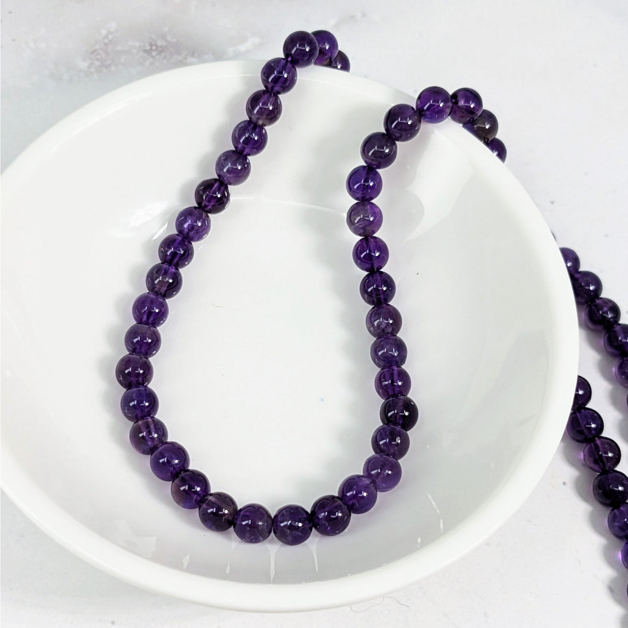 Amethyst 4 mm round beads on a white plate on a white table, 12 pack #LV3615