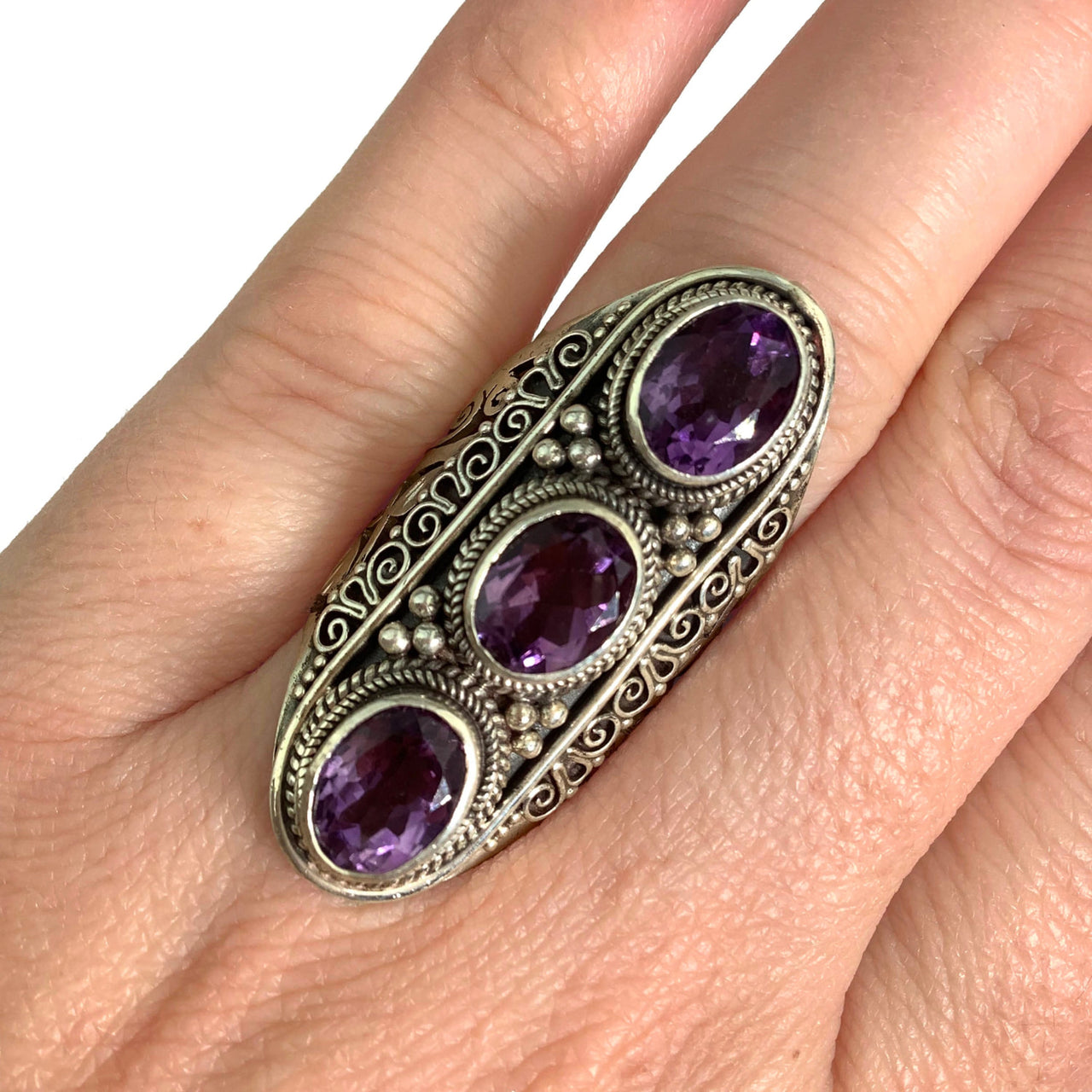 A woman’s hand holding Amethyst Faceted Triple Ring Size 8 with two oval amethyst stones