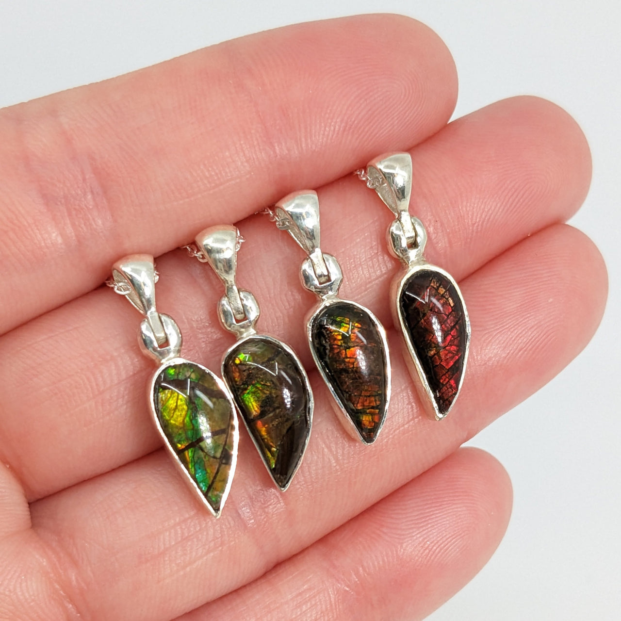 Hand holding Ammolite 18’ Sterling Silver Pendant with three different colored glass pendants