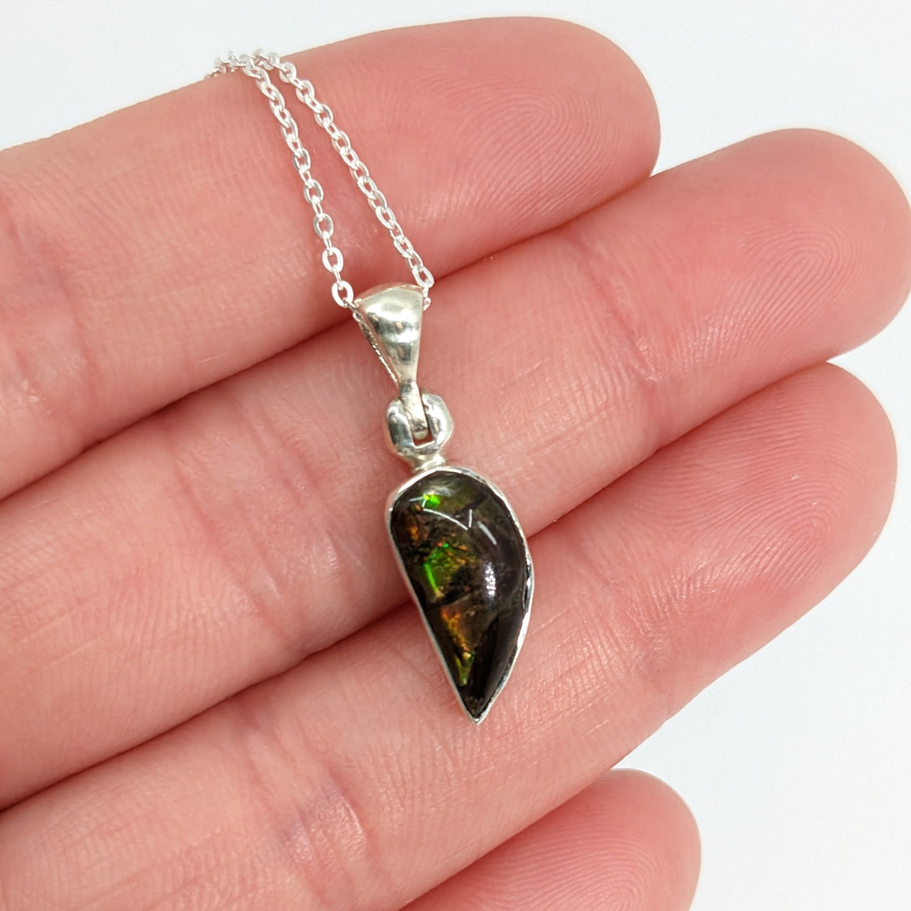 Person holding Ammolite 18’ sterling silver pendant with green stone (approx. 3g) #SK8914