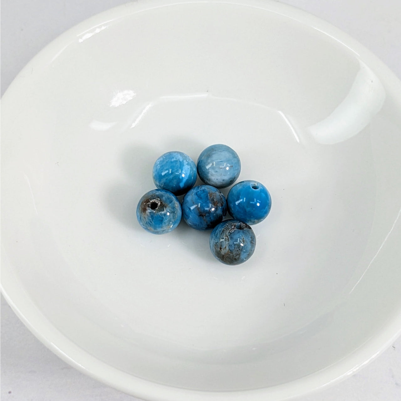 A white bowl filled with blue Apatite 7 mm Round Beads from the 6 pack #LV3628 product