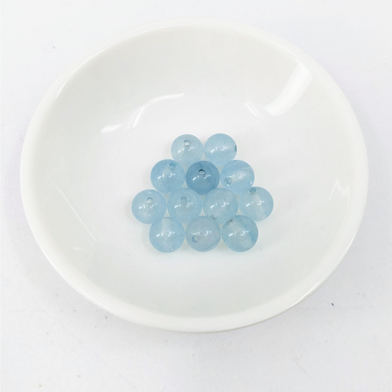 A white plate with blue glass pebbles from the Aquamarine 8 mm Round Bead 6 pack #LV3635