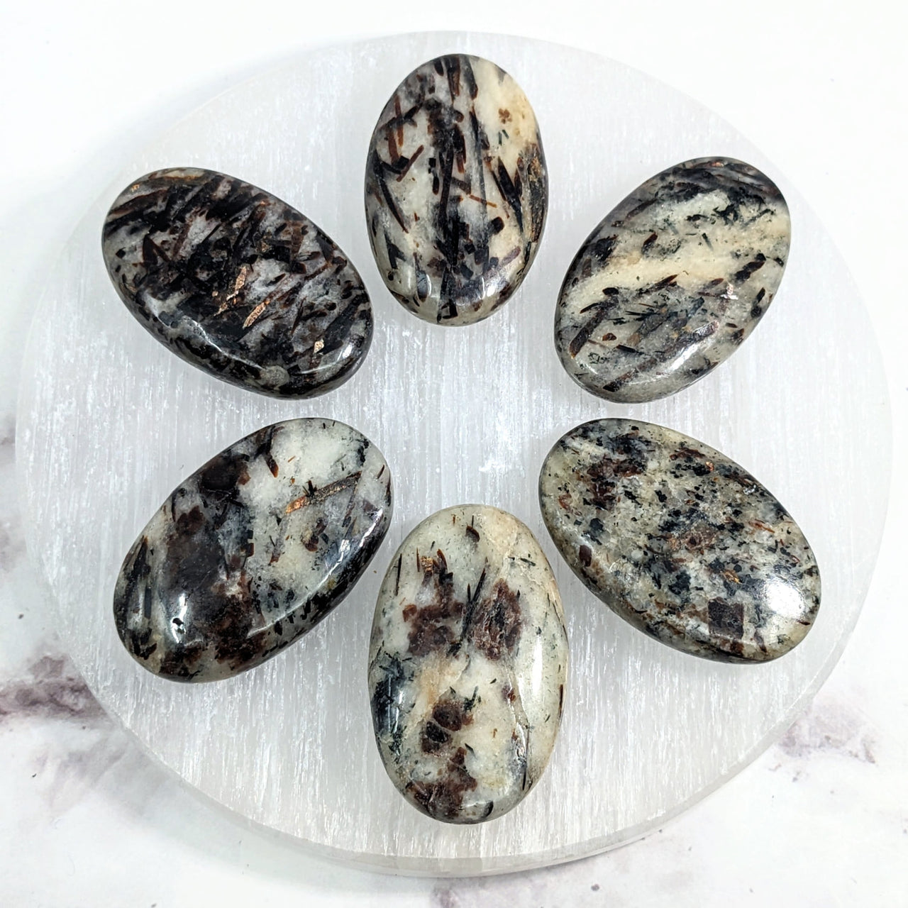 Astrophyllite Palm Stones: Six Black and White Stones on a White Plate, Marble Surface