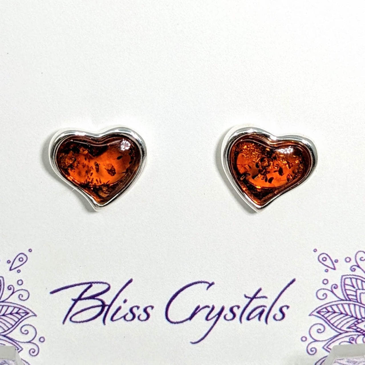 Pair of heart-shaped Baltic Amber stud earrings on a purple background (Product #LV1702)