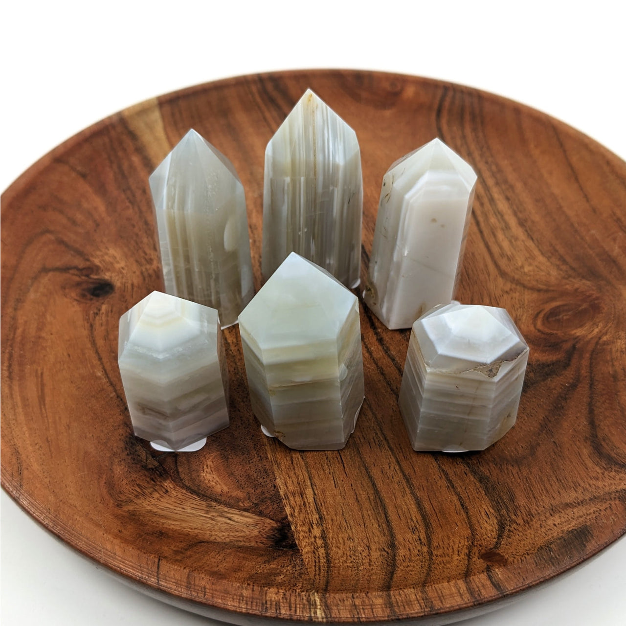 A wooden plate displaying five white quartz crystals alongside the Banded Agate Tower #LV2196