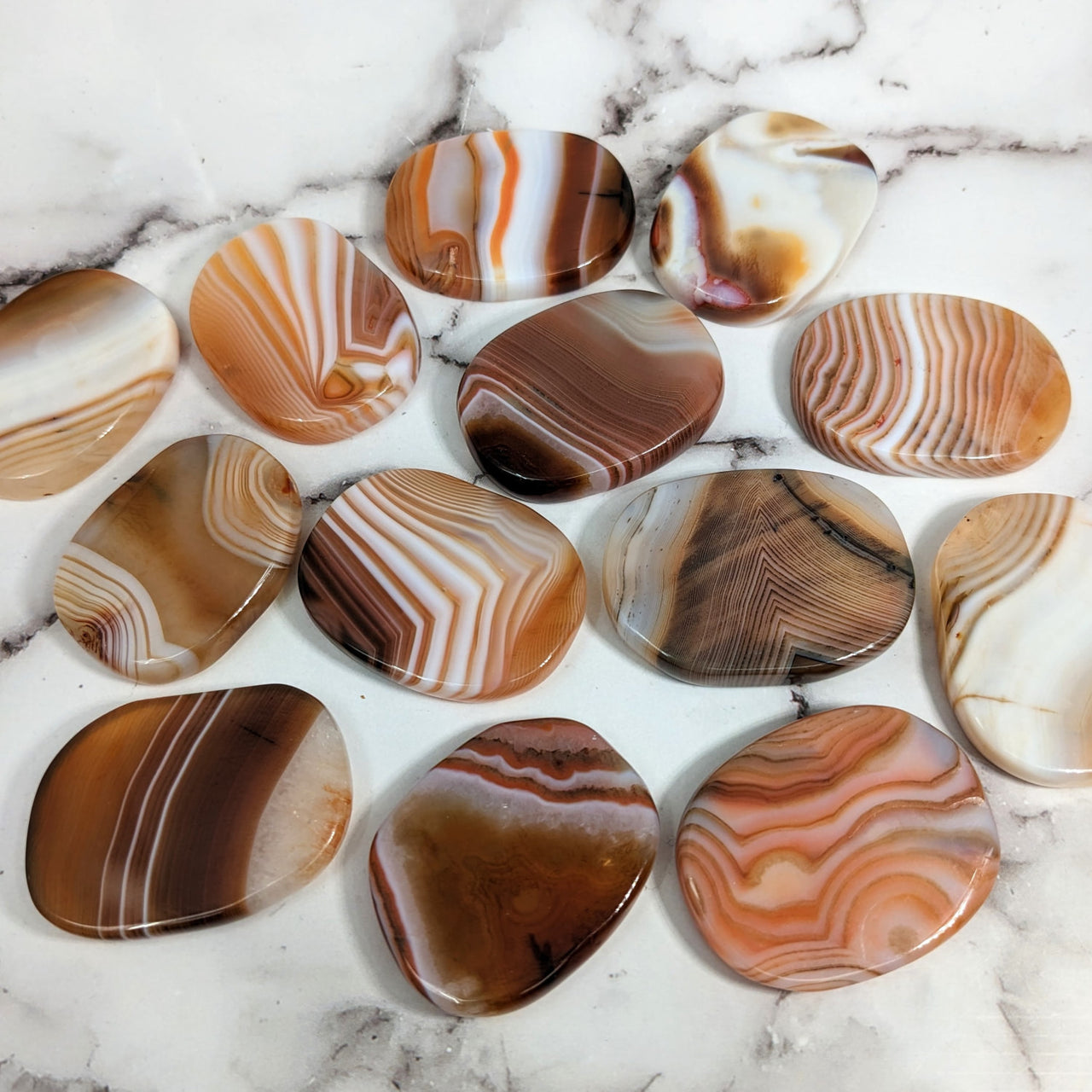 A pile of marble hearts on a marble table with Banded Carnelian Flat Palm Stones #SK8961