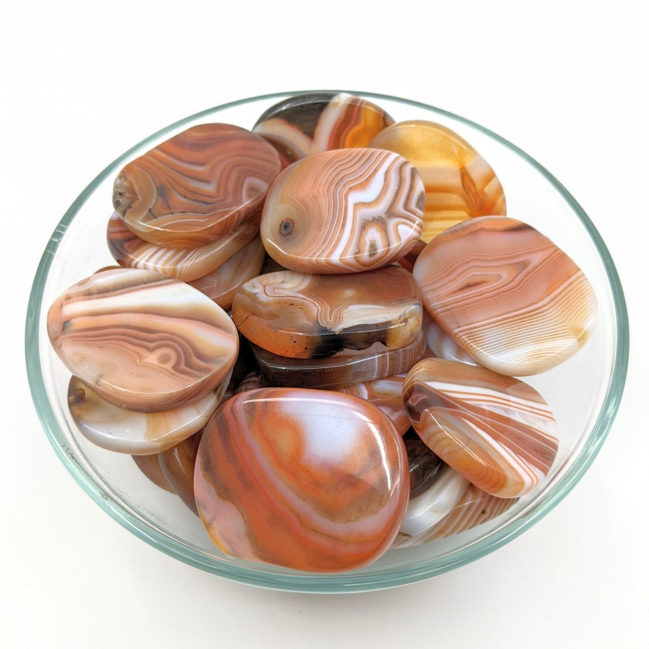 Textured glass bowl of assorted palm stones on a white surface #SK8961 Banded Carnelian