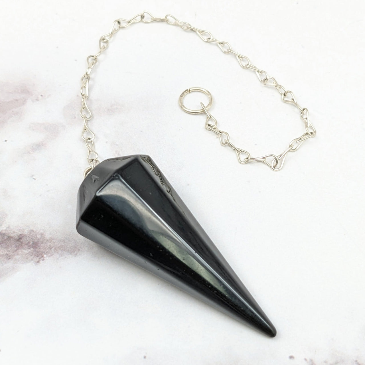 Black Obsidian Pendulum #J141: Close-up of a black cone on a chain on a marble surface