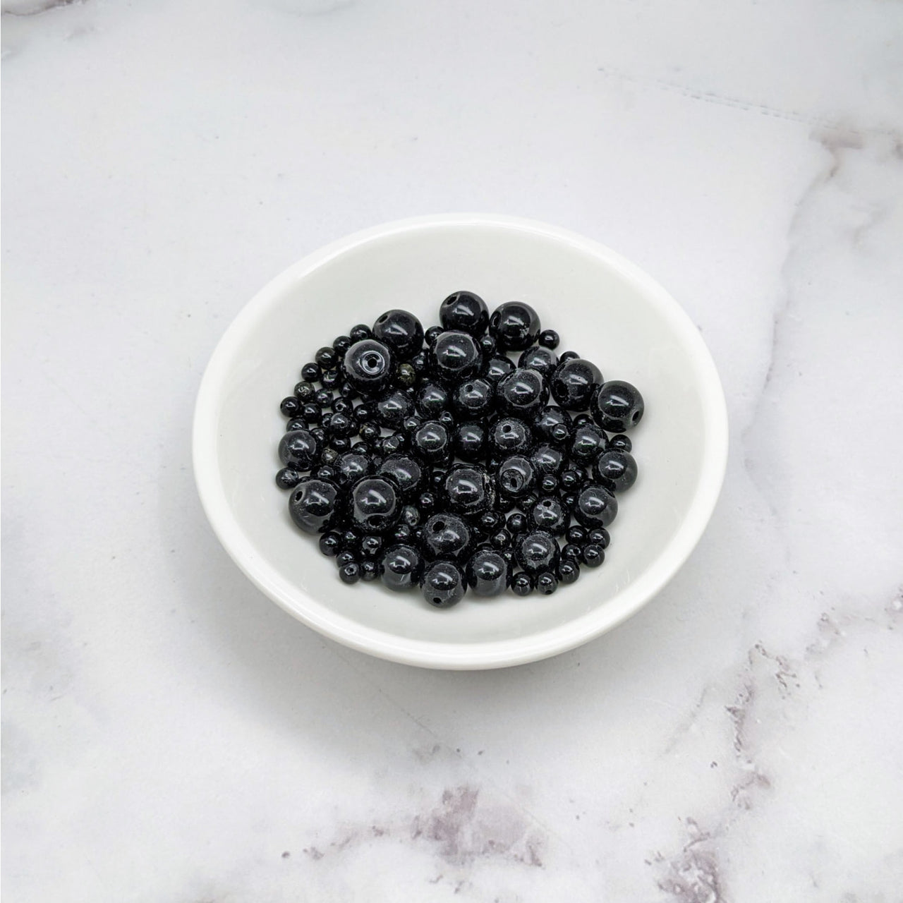 A bowl of blueberries on a marble counter showcasing Black Onyx Assorted Size Bead Pack #LV3652