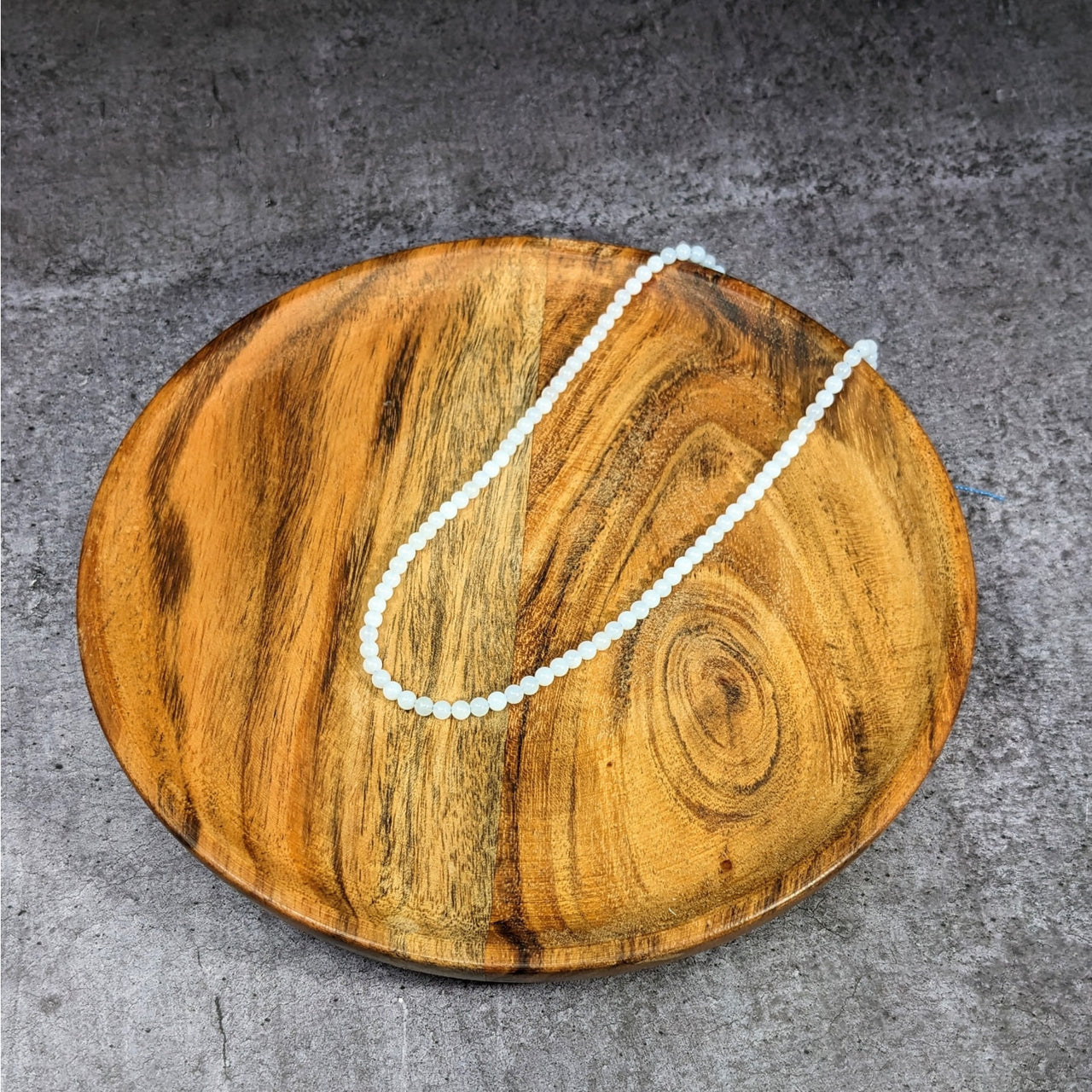 Wooden tray with a pearl blue chalcedony bead from the Blue Chalcedony 4 mm Round Bead Strand