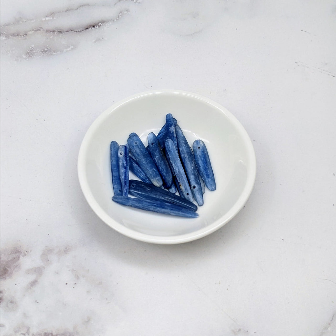 Blue kyanite chips on a white plate from Blue Kyanite Blade Top Hole Drilled Bead 12 Pack