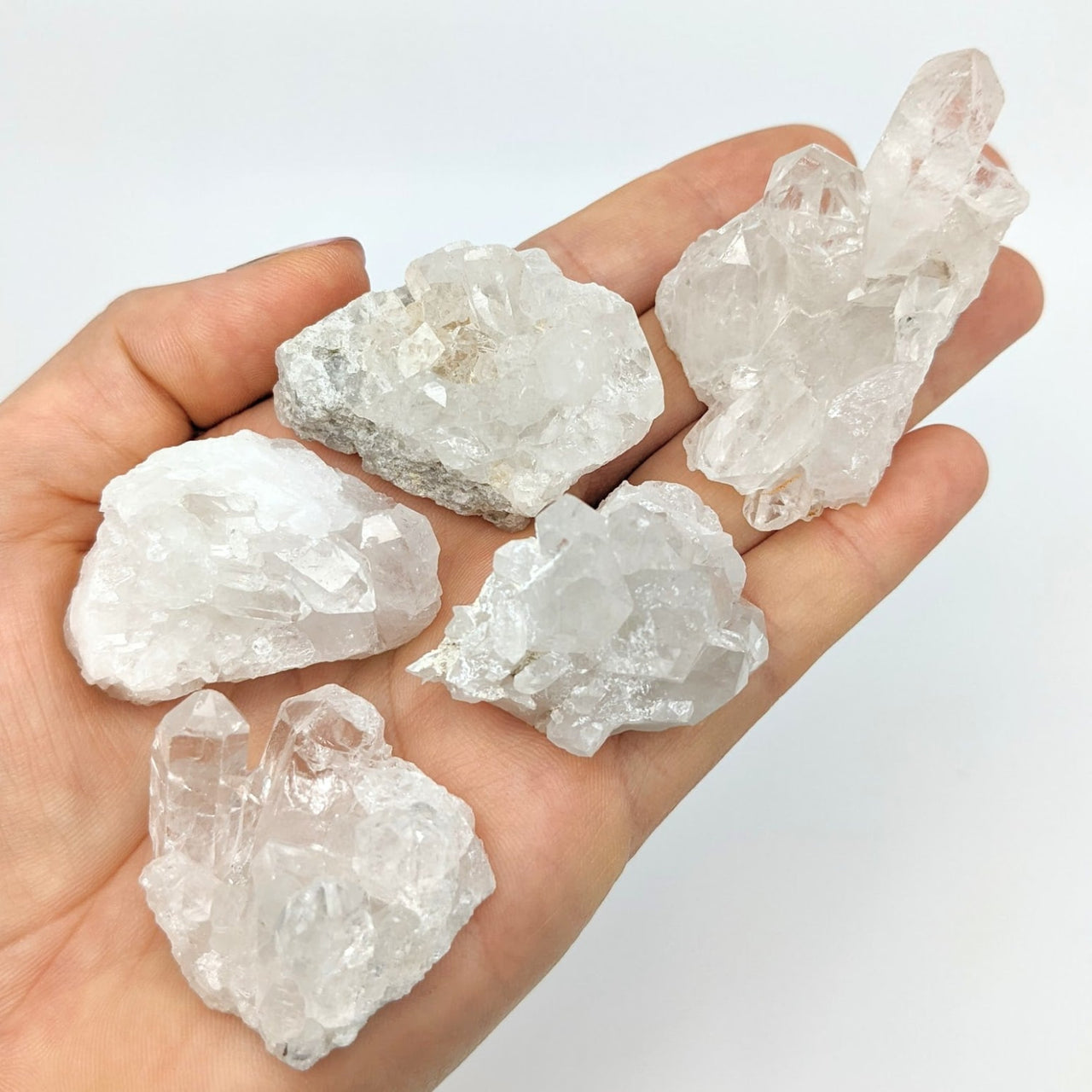 A hand holding five clear quartz crystals from the Clear Quartz 1.5’ Mini Cluster collection