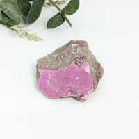 Thumbnail for Cobaltian Calcite 2.3’ Rough Specimen #LV2476 with a pink rock and plant in the background