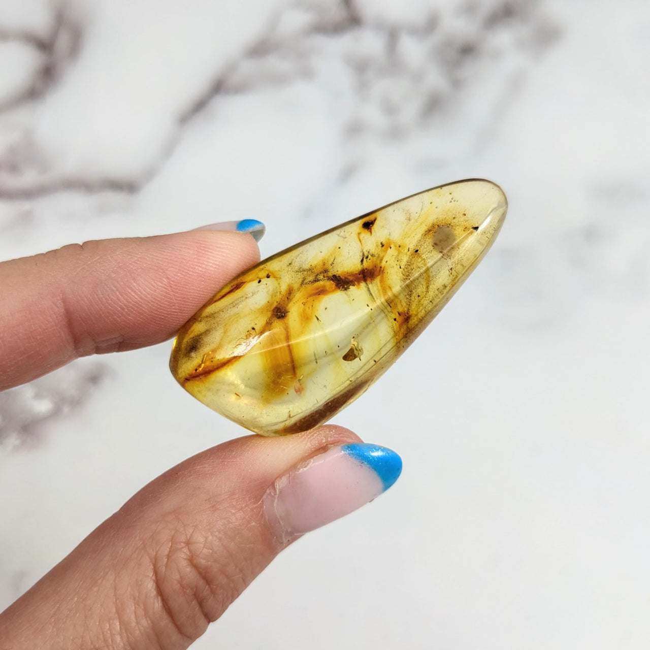 Person holding Colombian Amber 1.9’ polished piece #LV3158 with a brown substance inside