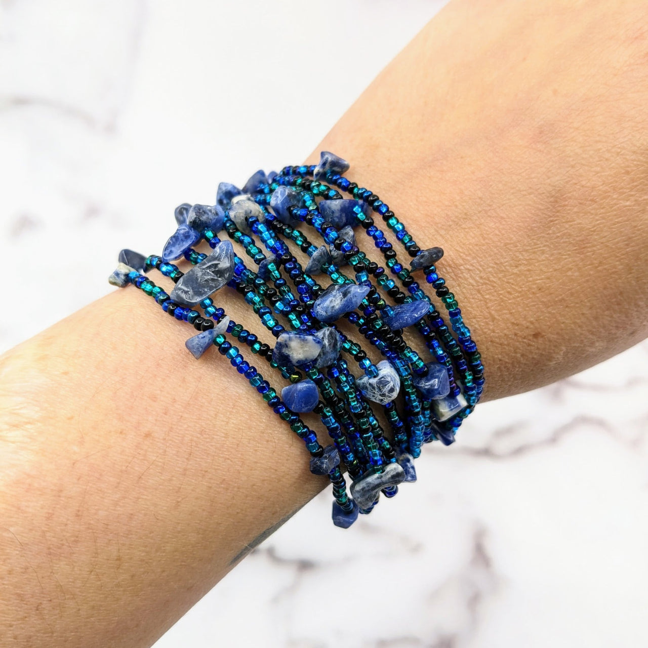 A woman’s arm wearing the Crystal Beaded 12 Strand Bracelet #LV1805 with blue beads and magnet clasp