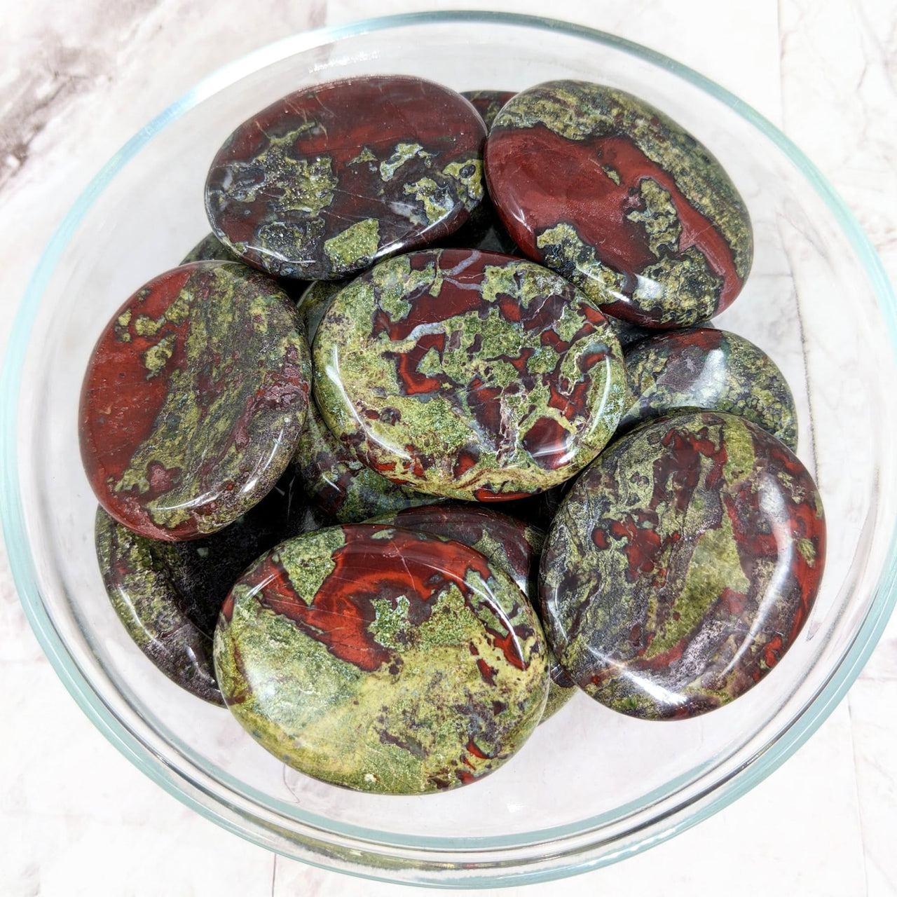 Dragon’s Bloodstone Thumb Stone with Palm Stones in a bowl filled with pest-covered pests