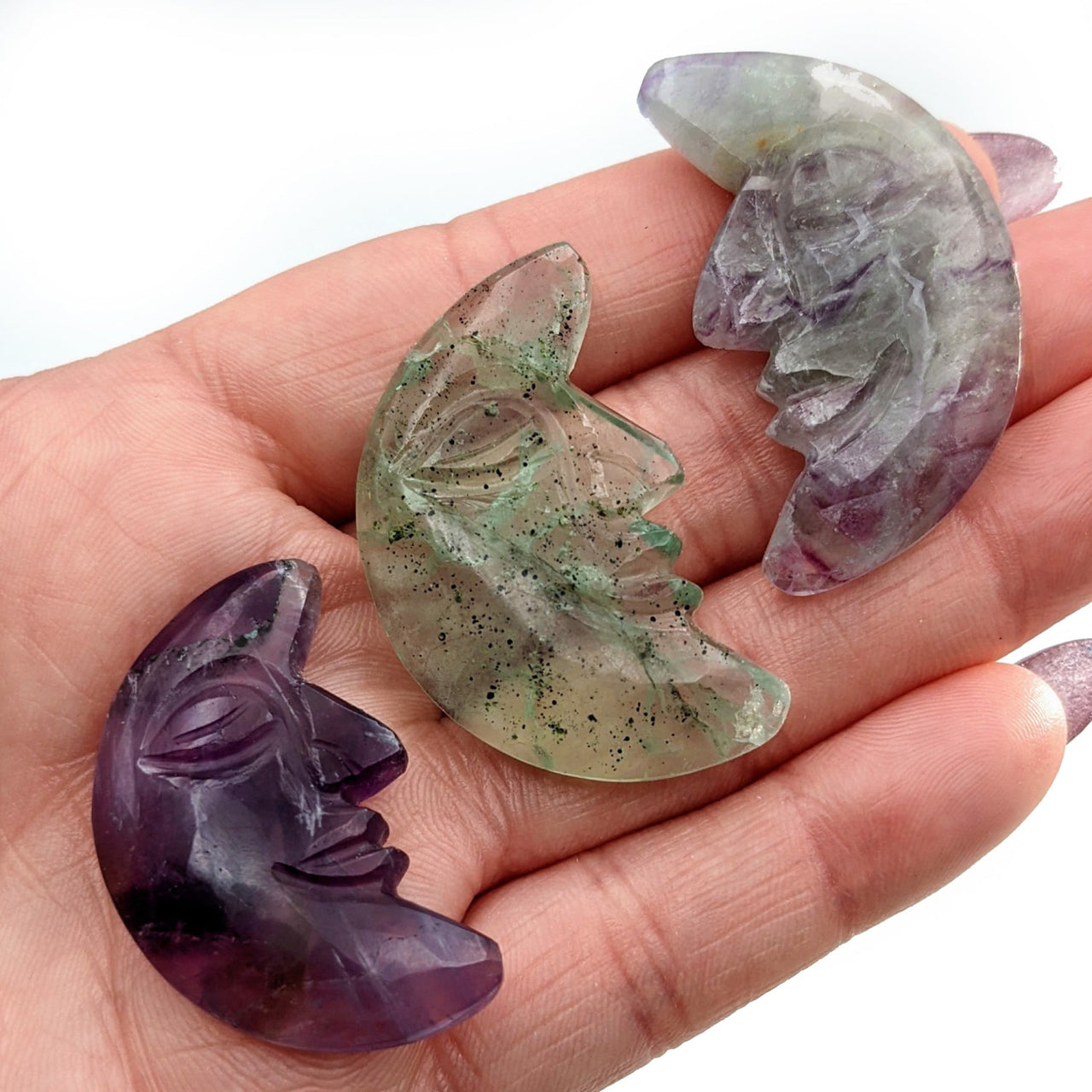 Hand holding three amethytes with Fluorite Carved Moon w Face #SK5939 in background