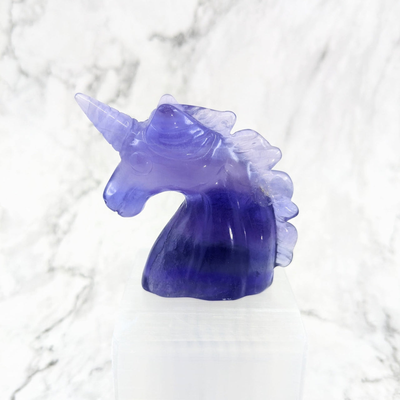 Purple glass unicorn head carving on white marble background, product: Fluorite Unicorn