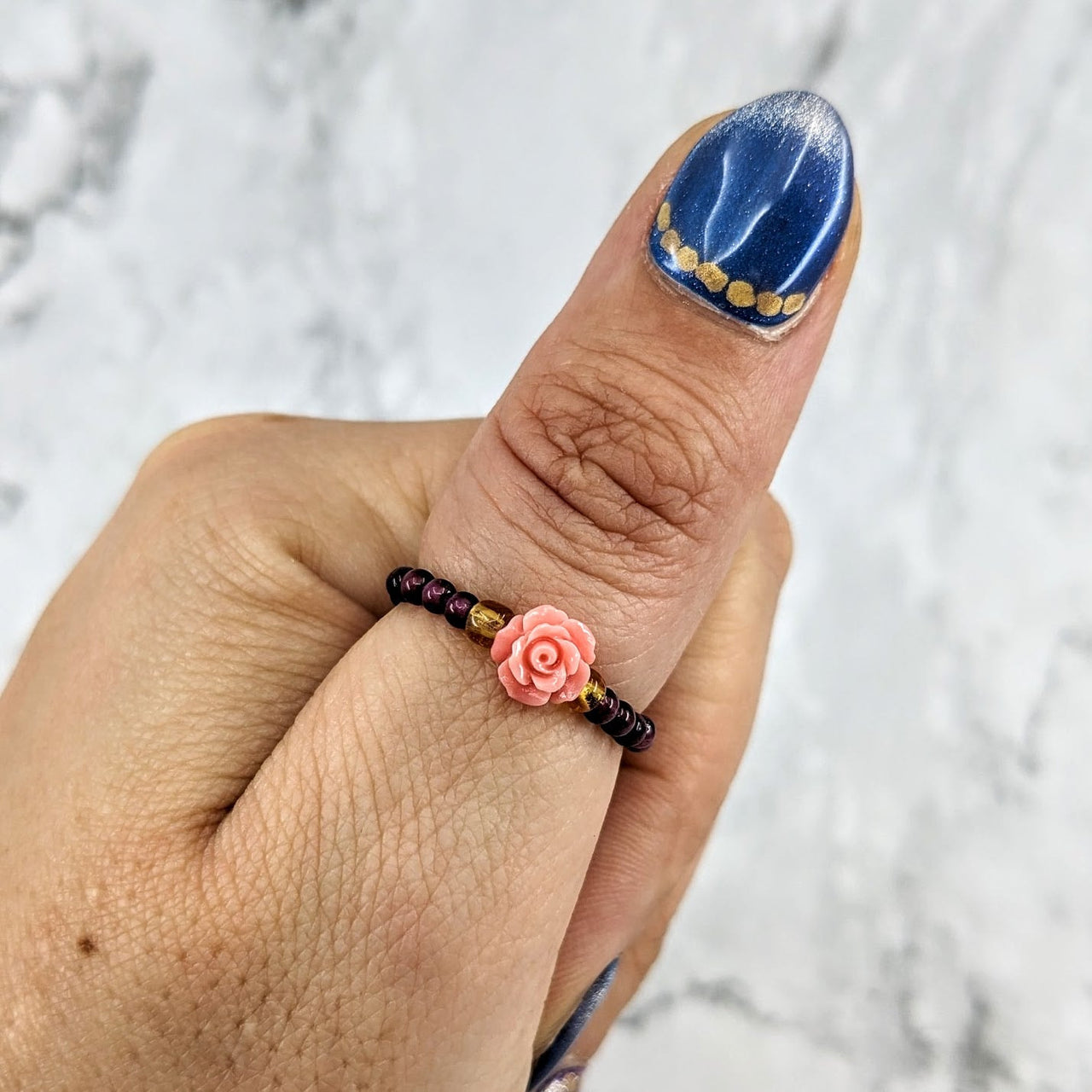 A woman’s hand with blue and white manicure featuring a rose, wearing Garnet Flower Beaded Ring