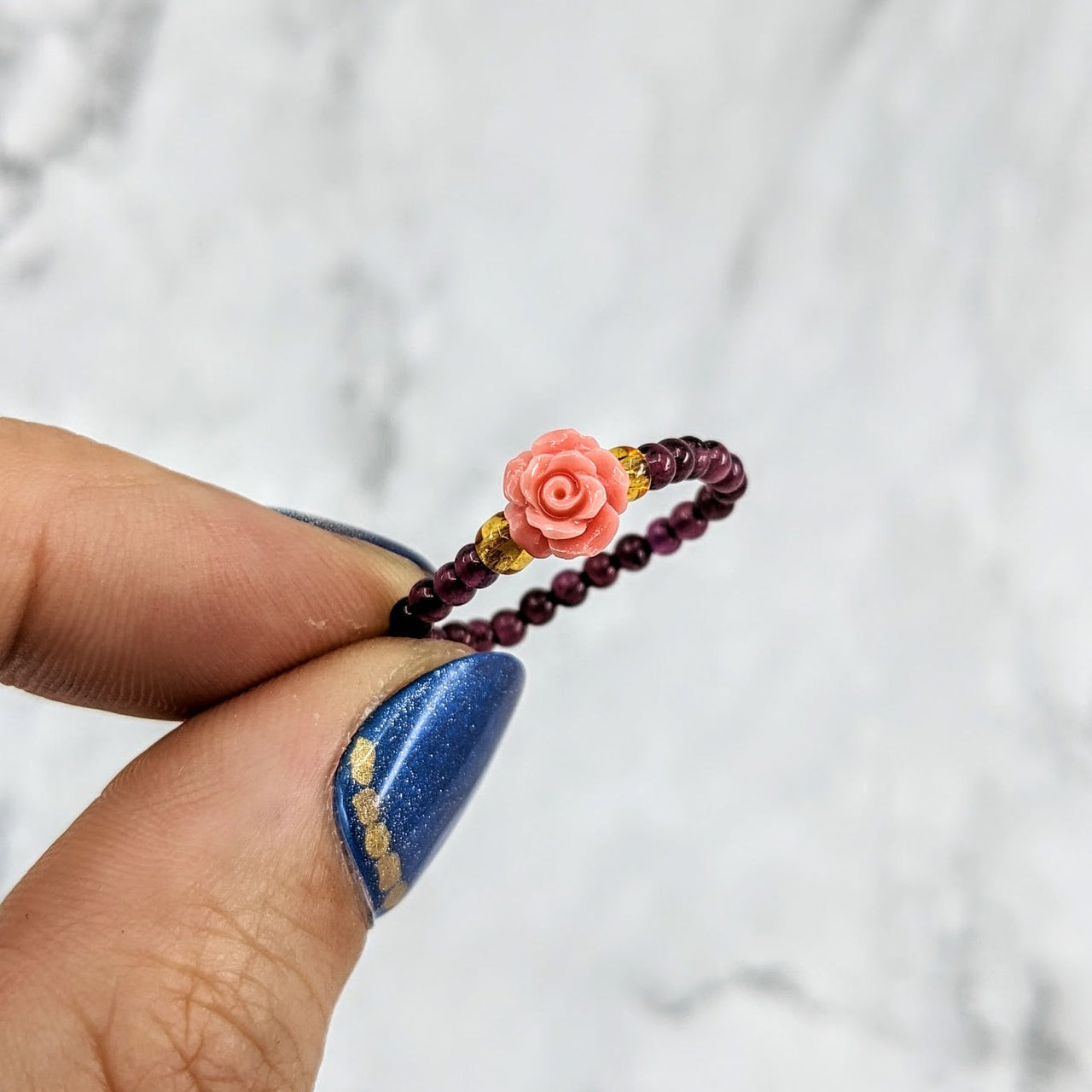 Hand holding a flower-shaped beaded ring named Garnet Flower 1’ Beaded Stretchy Ring #LV1971