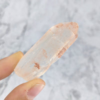 Thumbnail for Close-up of hand holding Hematoid Quartz rough point on marble surface