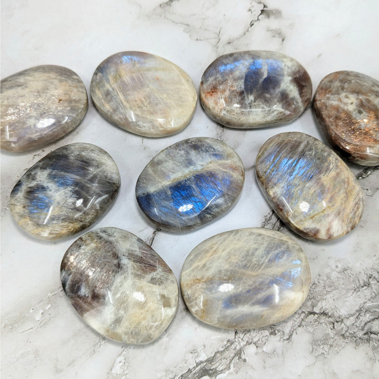 Close-up of Iridescent Sunfire 2’ Moonstone Palm Stones on Marble Surface – LV4064