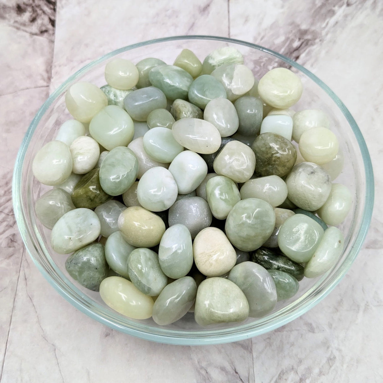 A bowl filled with pastel green jade tumbled stones, perfect for crystal enthusiasts