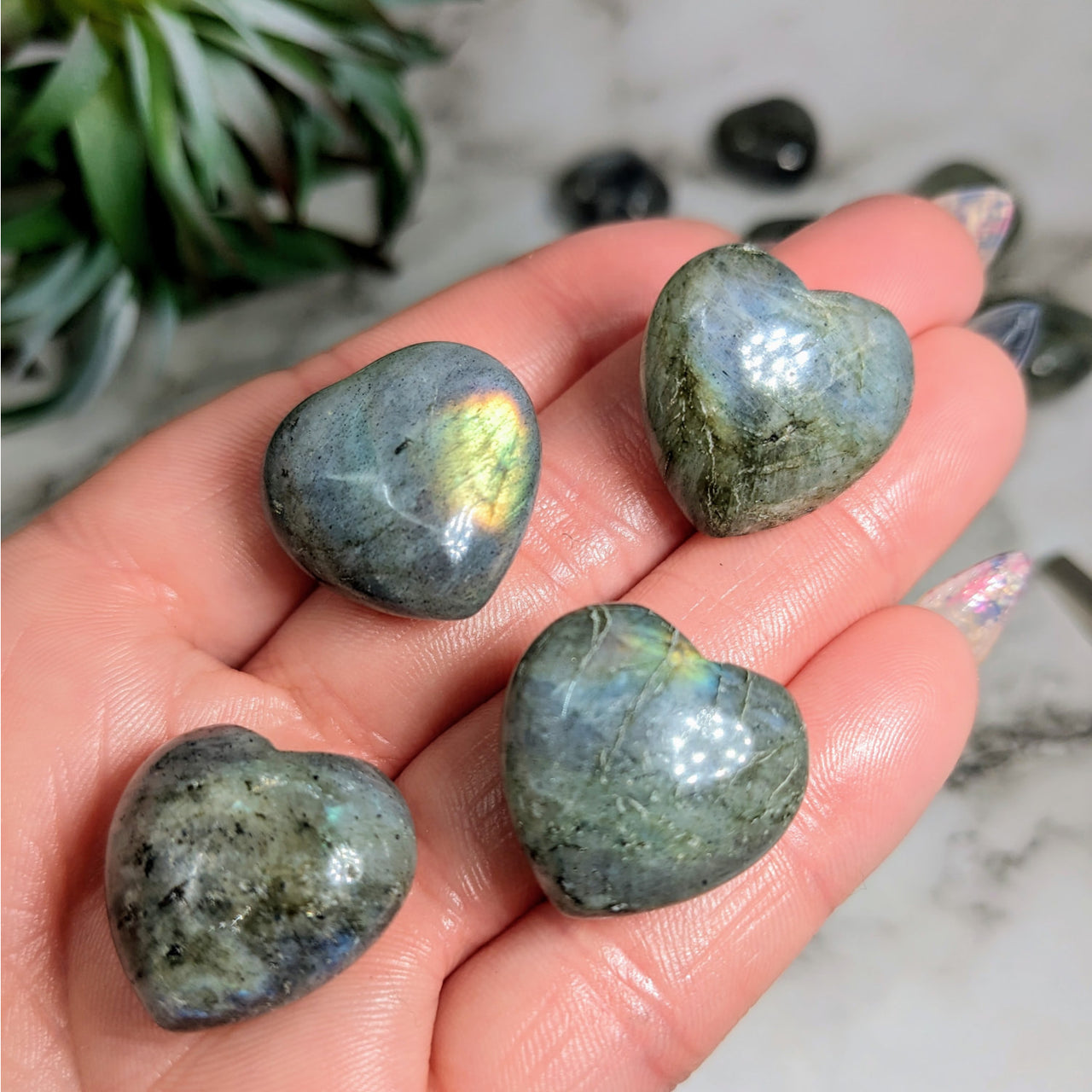 Three polished Labradorite stones in hand, showcasing ’Labradorite Mini Heart #LV4773’