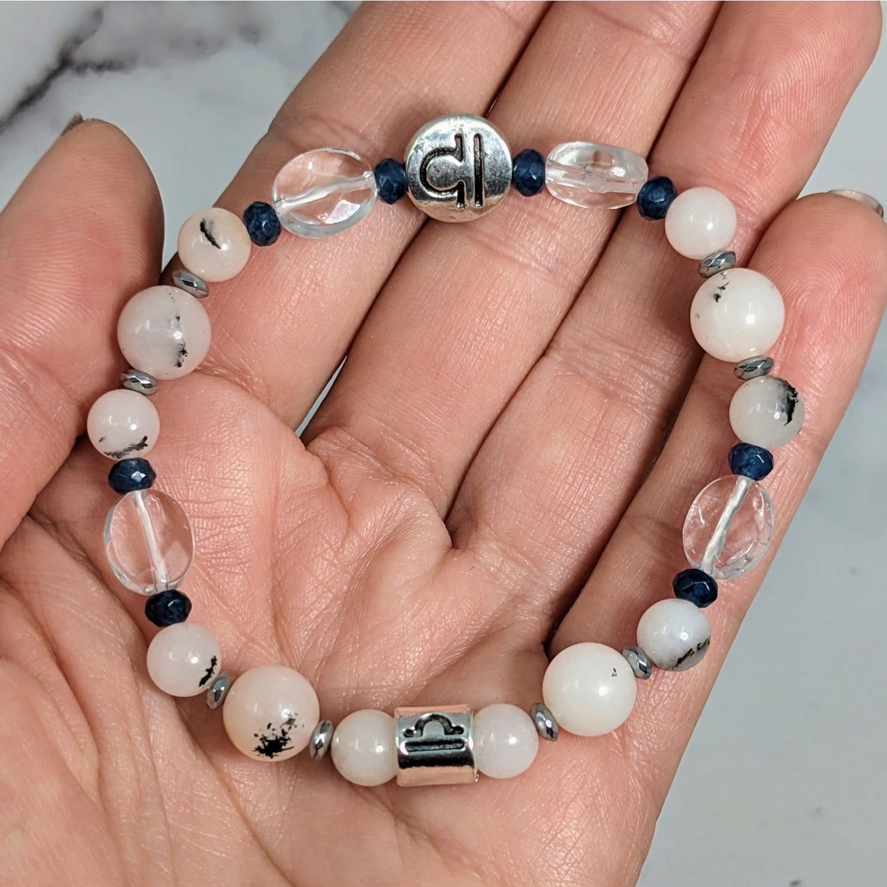 Person holding Libra Zodiac Handmade Beaded Bracelet with white and blue beads, 7 inches