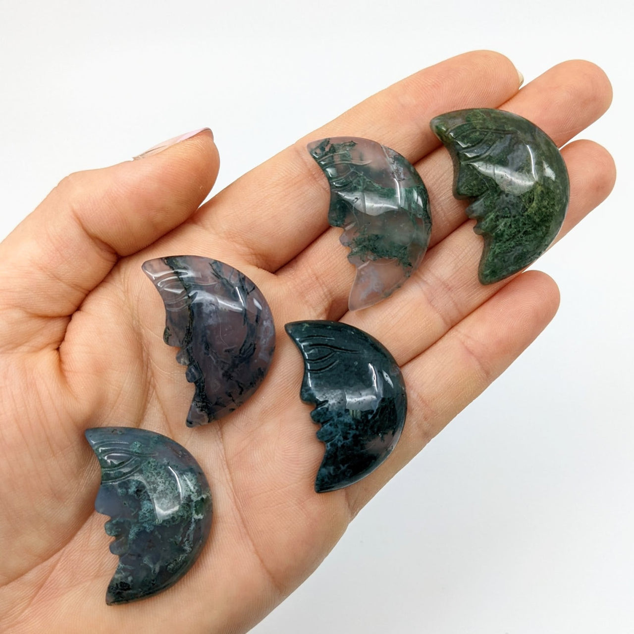 A hand holding three green and black marble pieces from Moss Agate Crescent Moon #SK9168