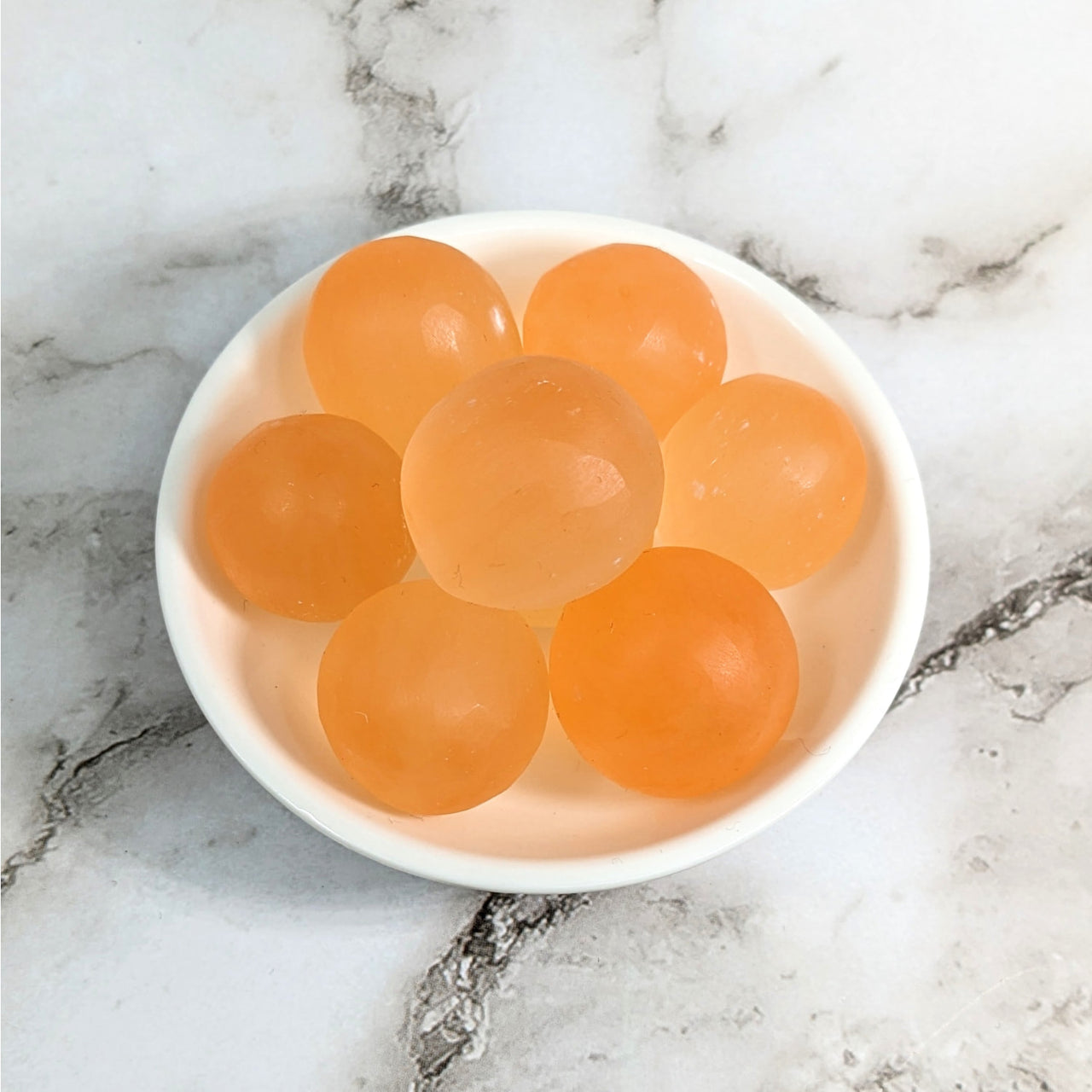 A bowl of orange tumbled stones on a marble counter, Peach Selenite .8 - 1’ #LV4137