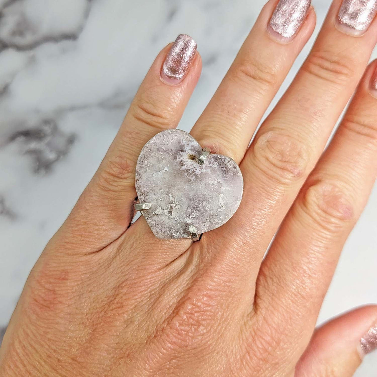 A woman’s hand wearing a Pink Amethyst Heart Adjustable Ring with a large white diamond