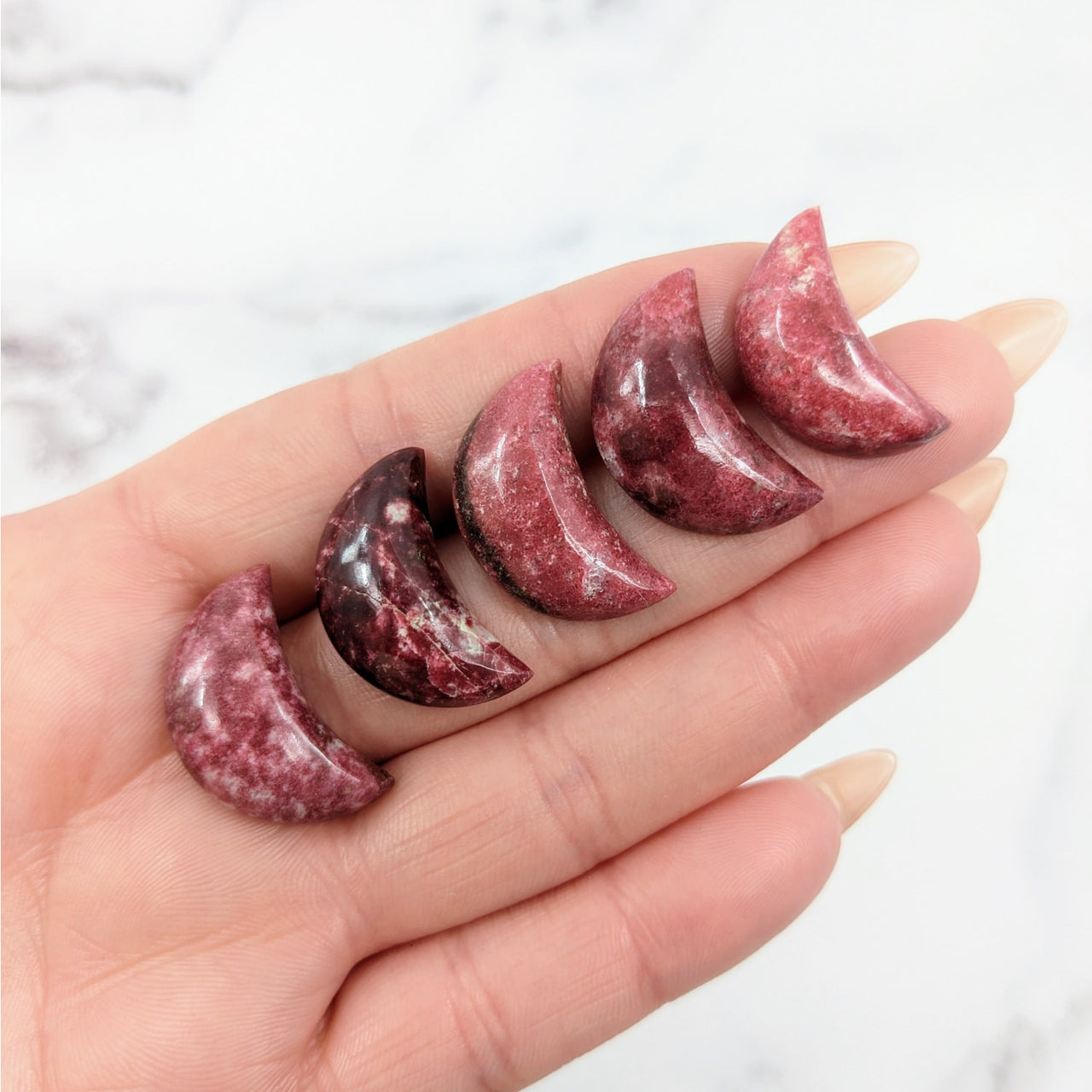 Hand holding three red marble pieces with Pink Thulite Crescent Moon #LV3921 in background