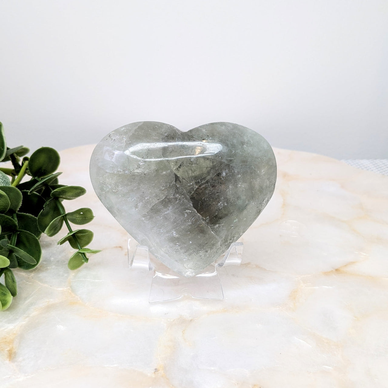 Heart-shaped quartz stone on white marble table from Prasiolite Jumbo Heart #LV4855