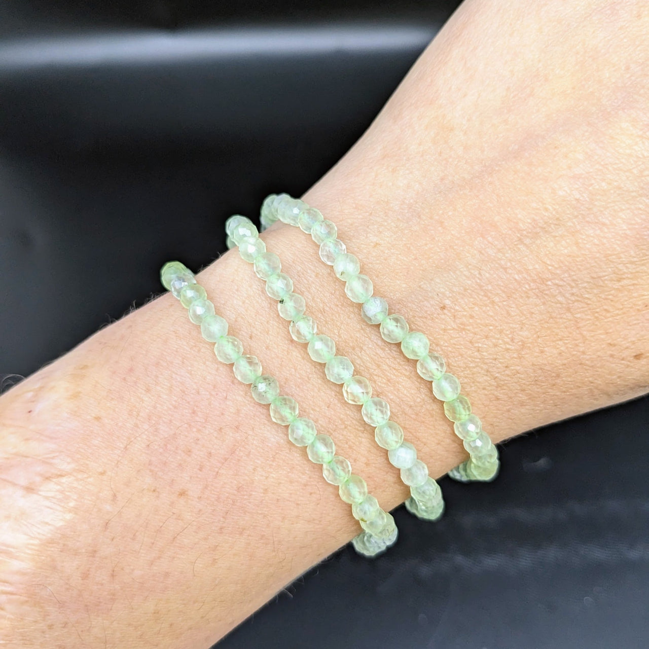 A woman’s arm adorned with Prehnite bracelet #LV1844, featuring faceted green quartz beads