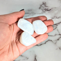 Thumbnail for Hand holding two heart-shaped white sea glass tumbled stones from Rainbow Ice Moonstone