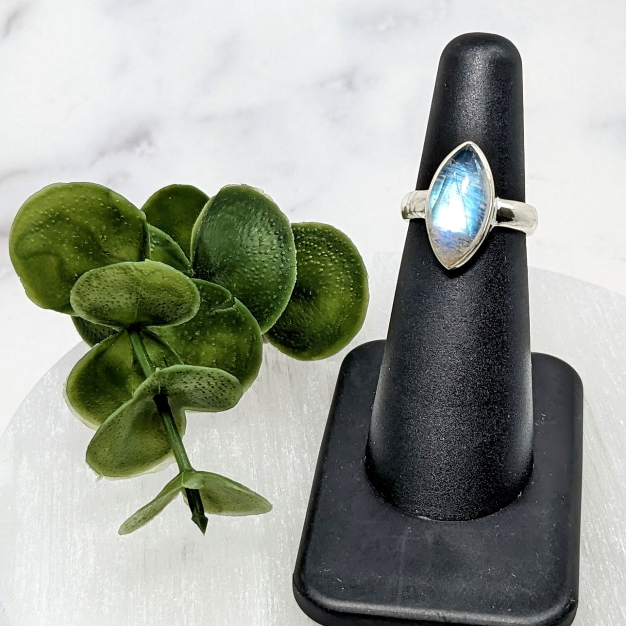 Rainbow Moonstone S.S. Marquis Ring #LV3963 with blue topaz stone on a black stand