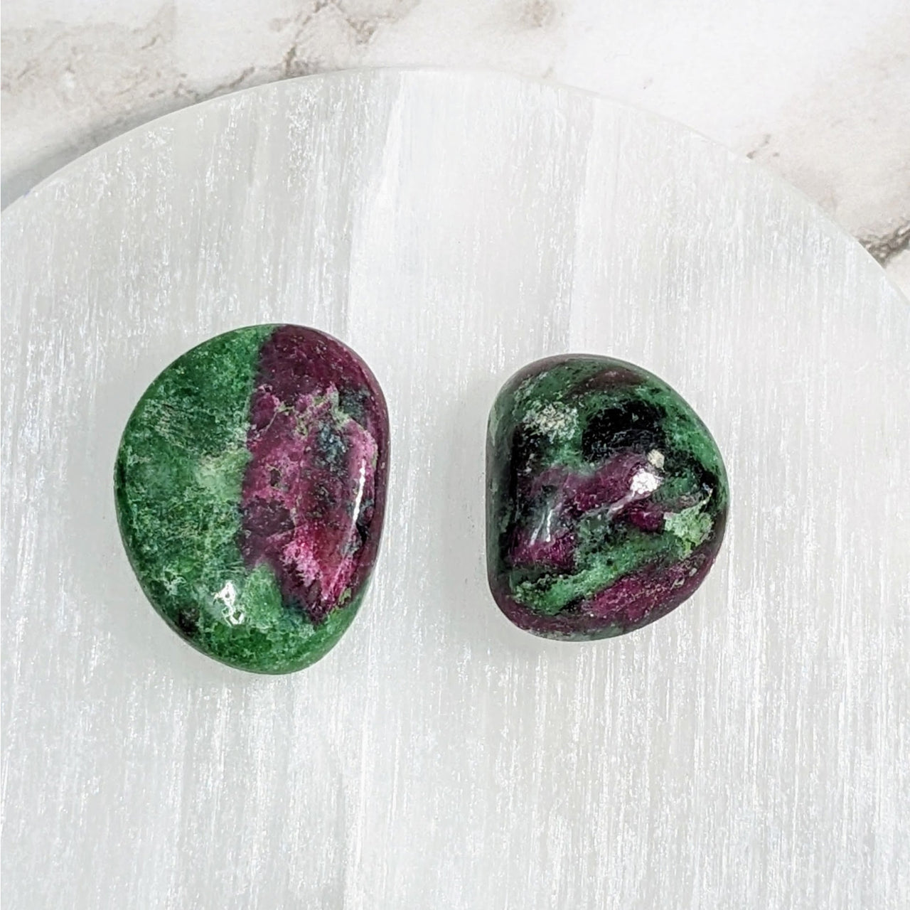 Two green and purple tumbled stones on a white marble table, Ruby Zoisite 1-1.2’ #LV4055