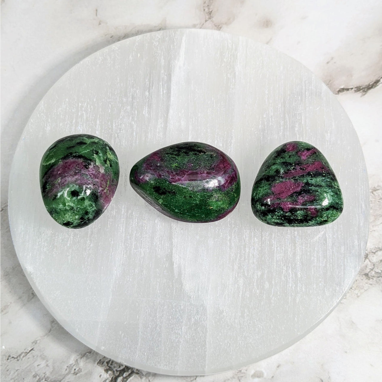 Tumbled stones: Three green and purple Ruby Zoisite on a white marble surface