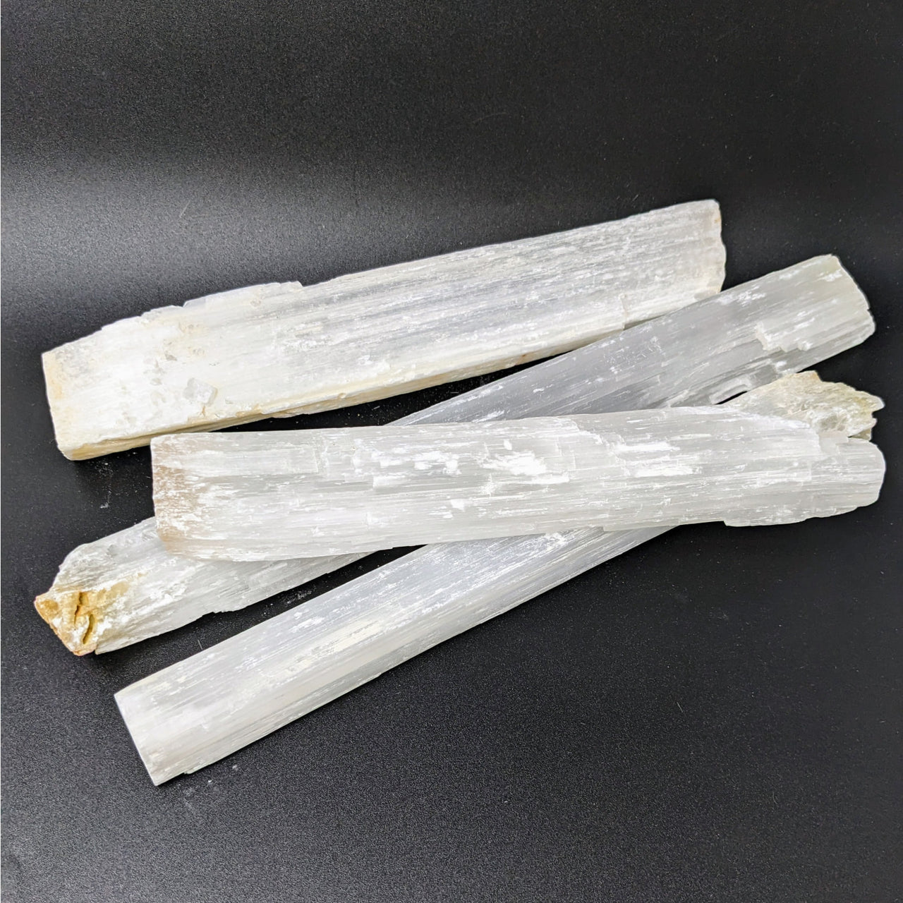 Three white quartz crystals on black surface - Selenite Rough Jumbo Wand #LV3399