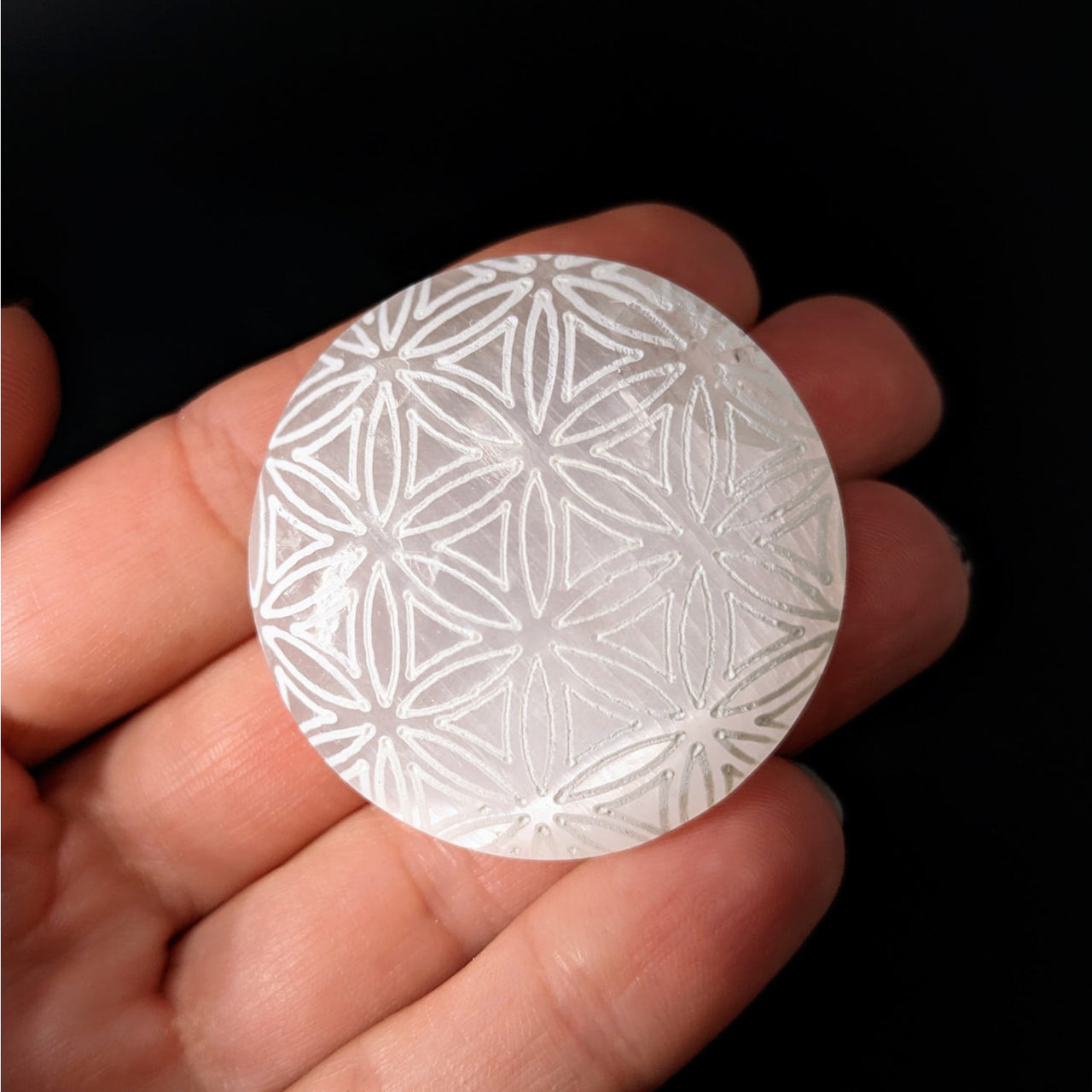 A person holding a Selenite Etched 1.5’ Flower of Life Palm Stone #LV4132 in their hand