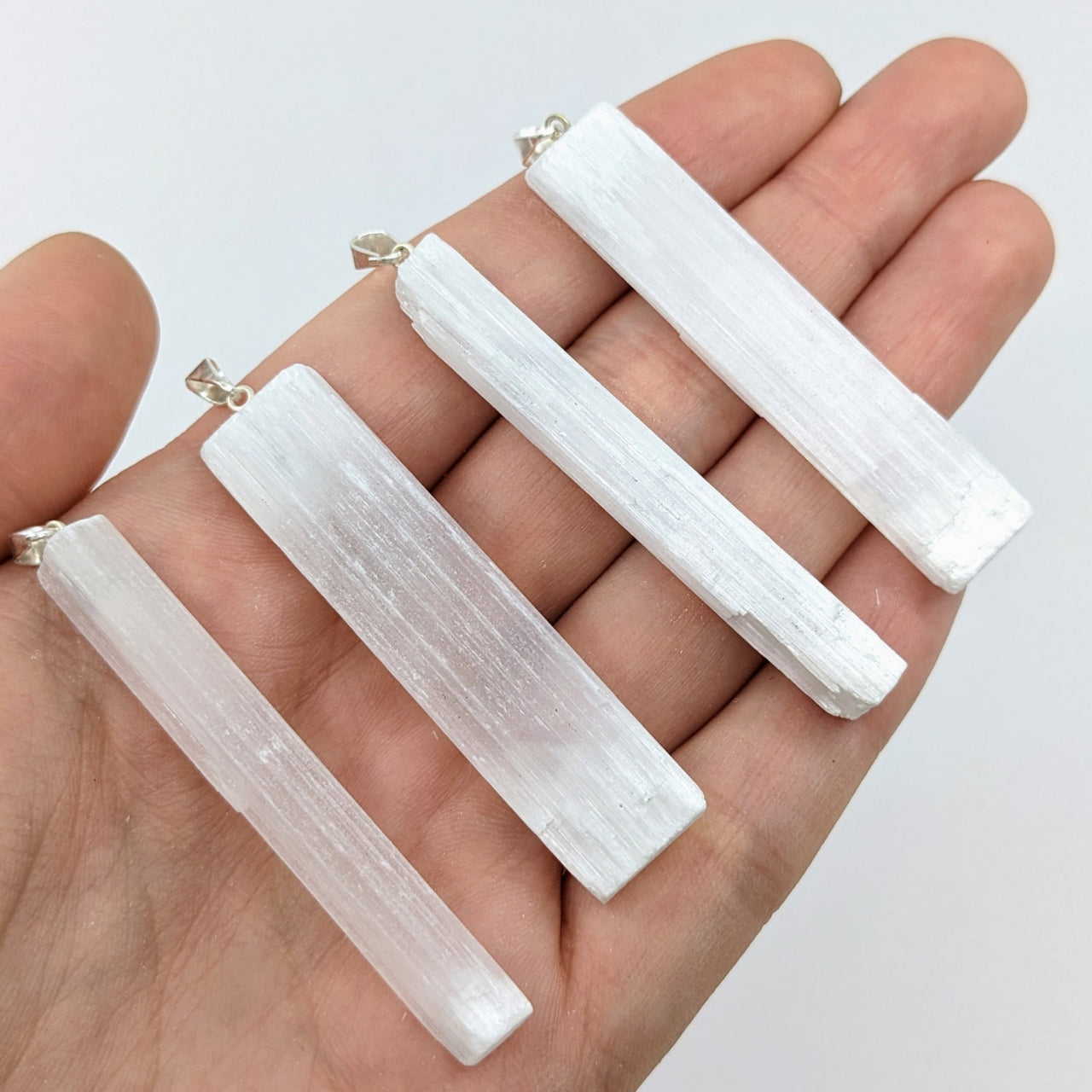 Close-up of a hand holding a Selenite Stick 2’ Pendant, product number LV2909