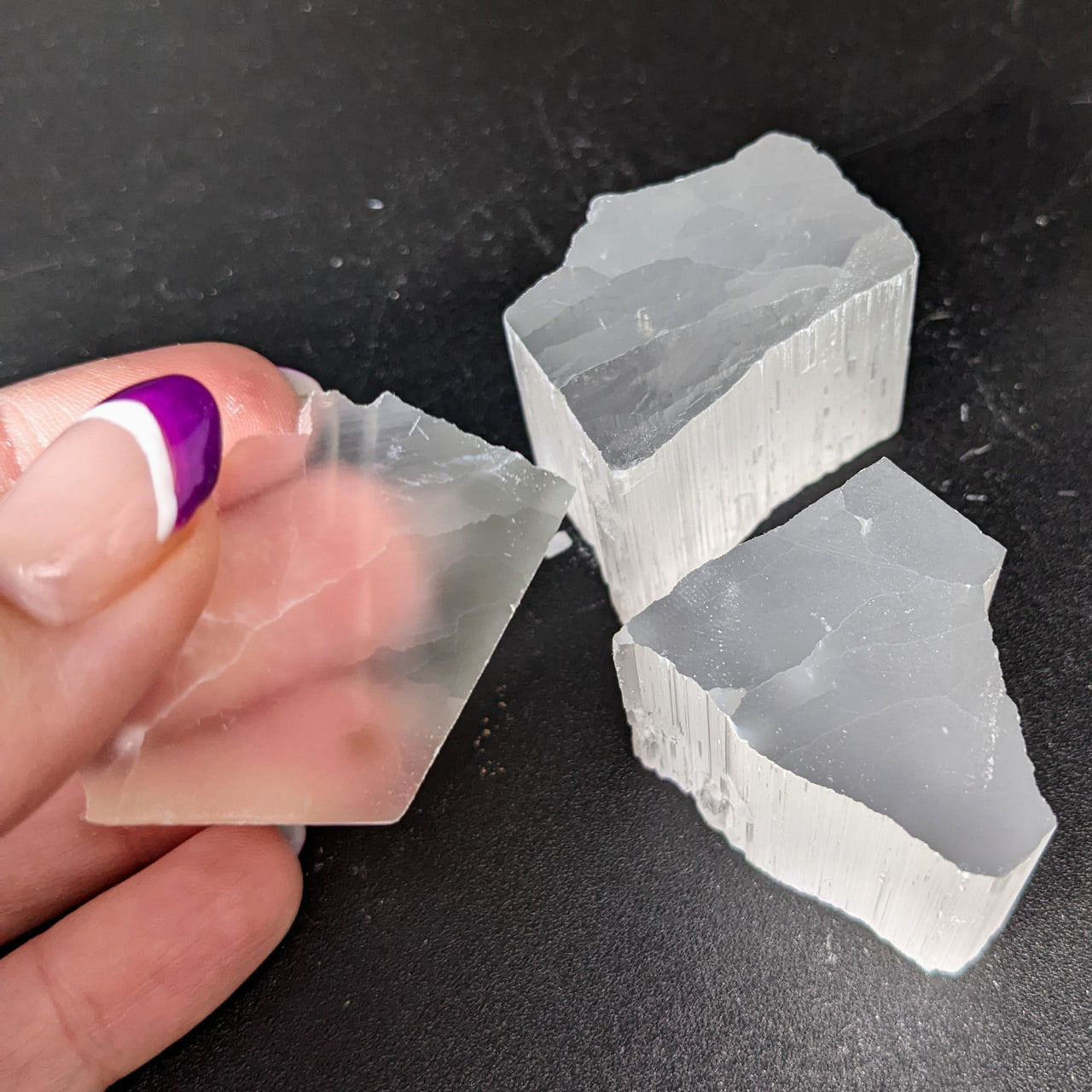 A hand with purple nails holding ice, displayed with Selenite TV Rock Rough #SK8746