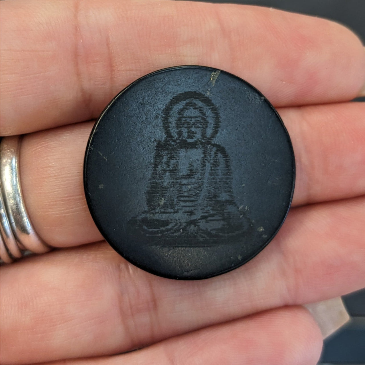 Person holding Shungite Buddha Adhesive Disc for EMF protection and cell phone enhancement