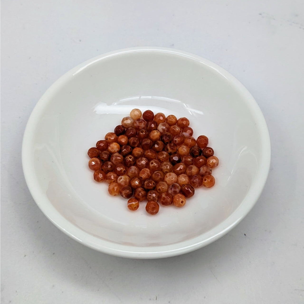 White bowl of red beans next to Snakeskin Agate Faceted 4mm Bead Pack LV3662