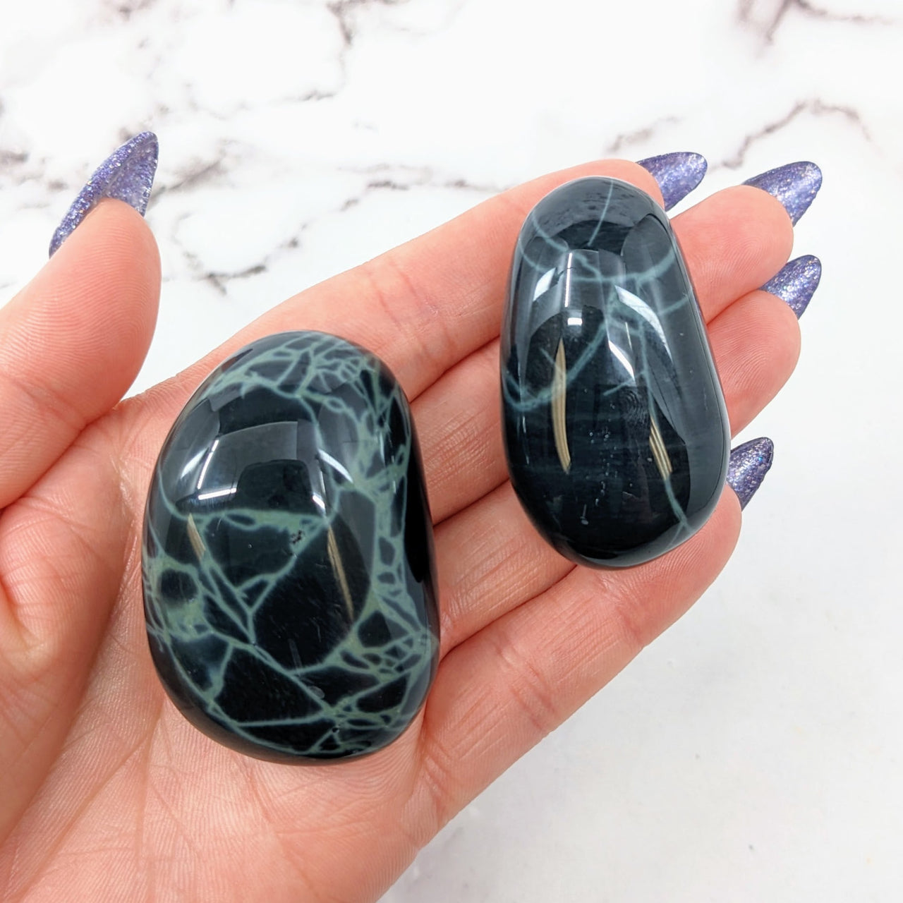 Obsidian Pebble #LV2743 showcased as two black and white marbles on a hand