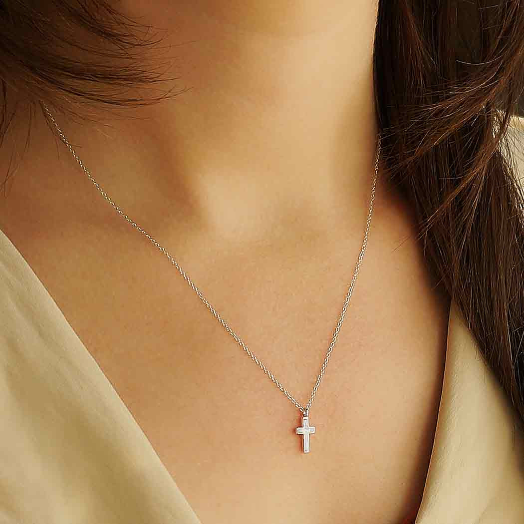 Woman wearing a sterling silver charm necklace with cross pendant from product #J033