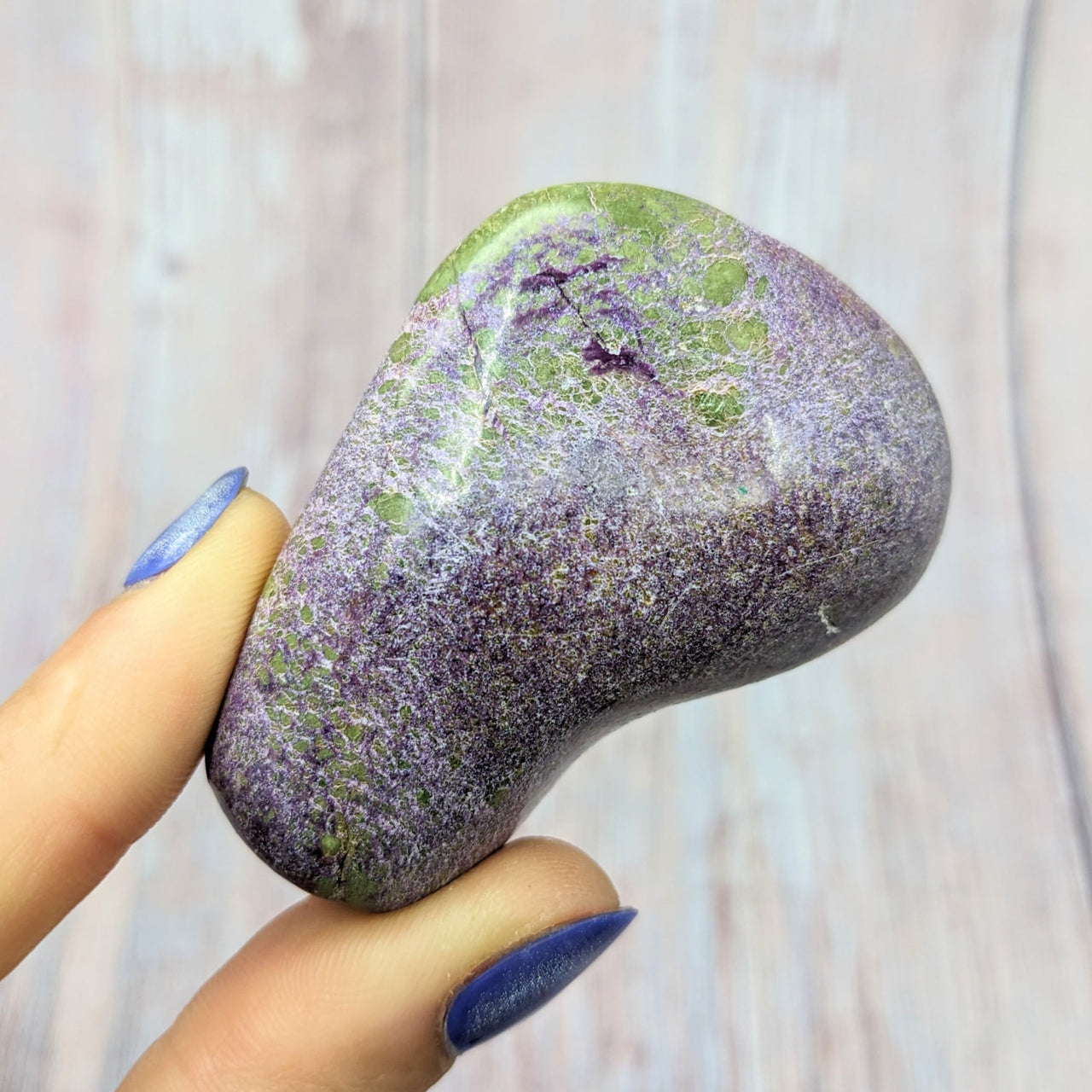 Hand holding Stitchtite Serpentine pebble with purple and green hues, SKU #SK9969