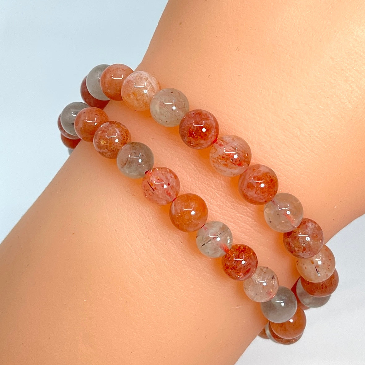 Close-up of a person wearing a Sunstone 7’ Bracelet with red and grey beads from Bliss Crystals